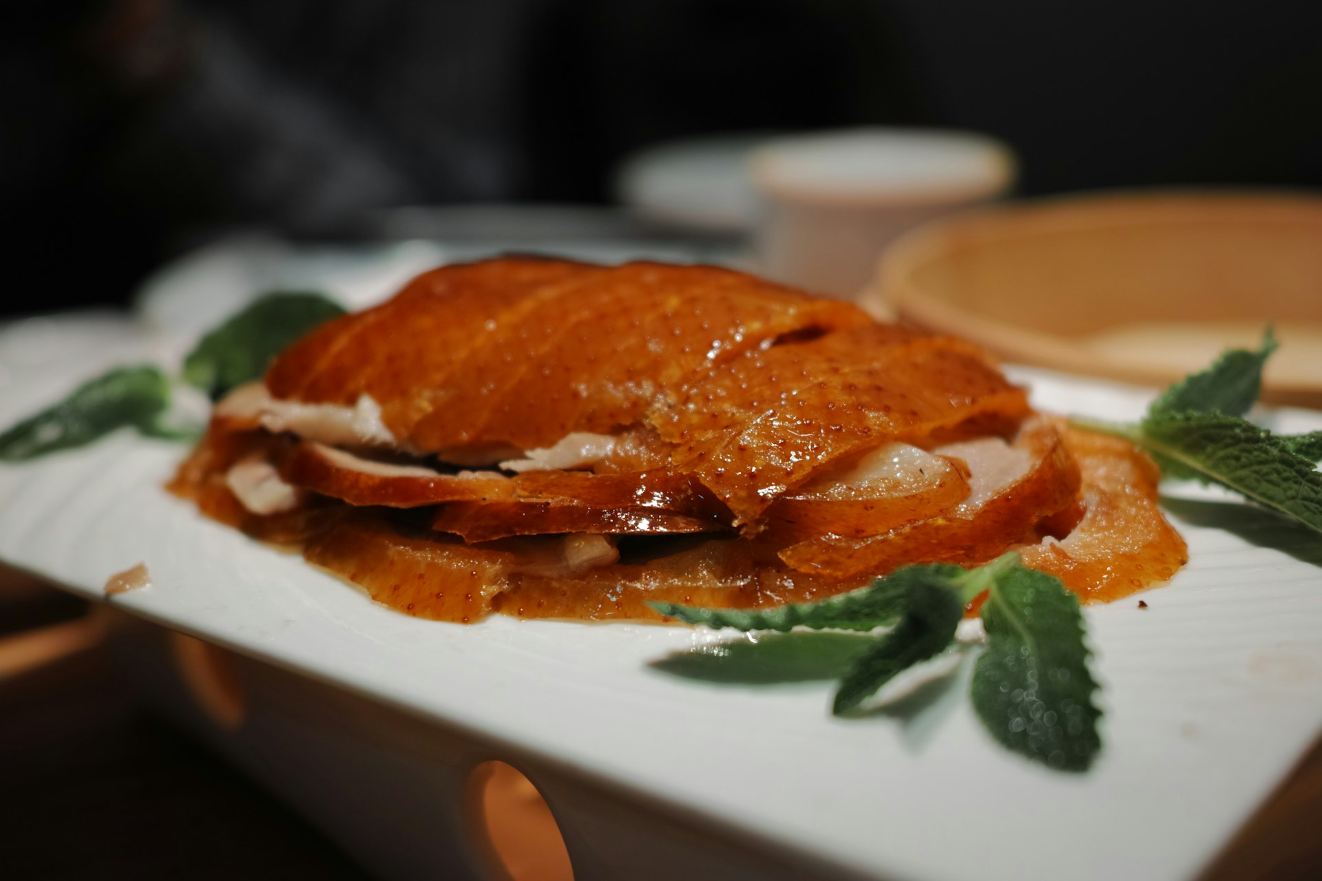 A chef carving glossy lacquered Peking duck tableside, thin pancakes, scallions and sweet bean sauce laid out