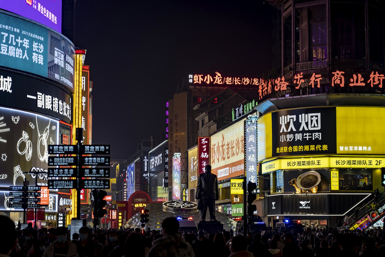 Huangxing Road pedestrian street in Changsha at night, with neon shop signs, a statue and crowds in the street