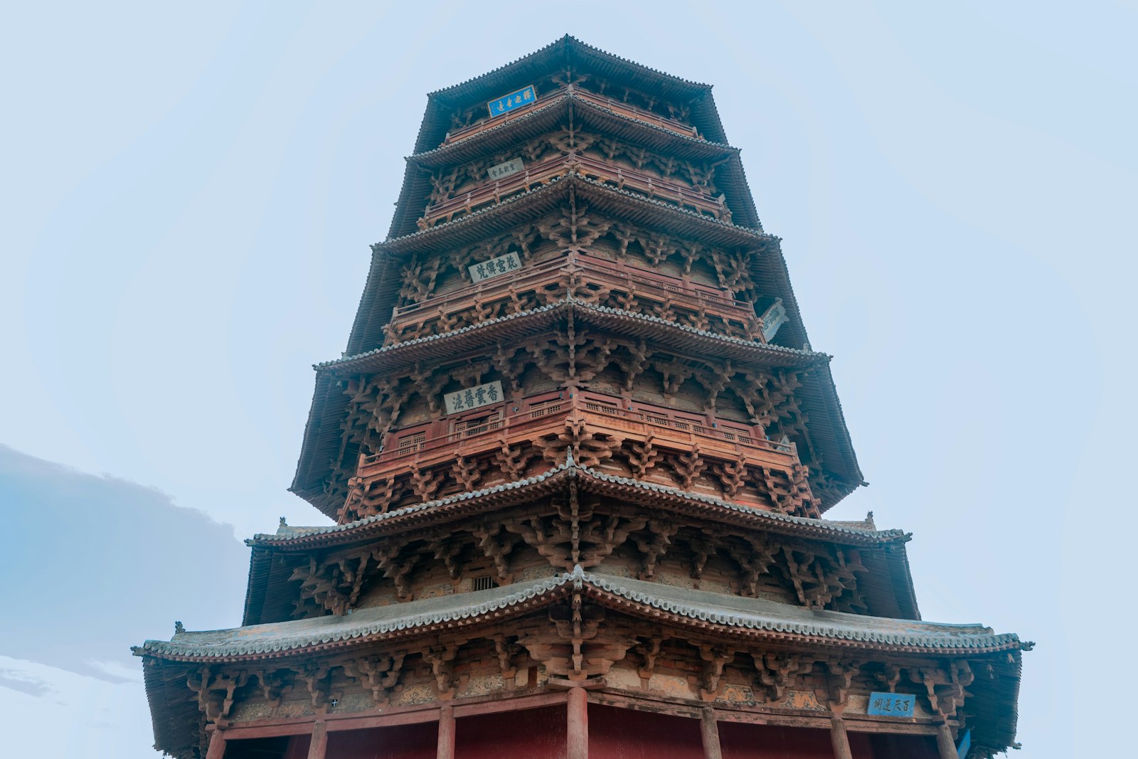 Looking up at the Yingxian Wooden Pagoda — tier after tier of tiled eaves and dense red-brown timber bracket sets rising against a pale sky