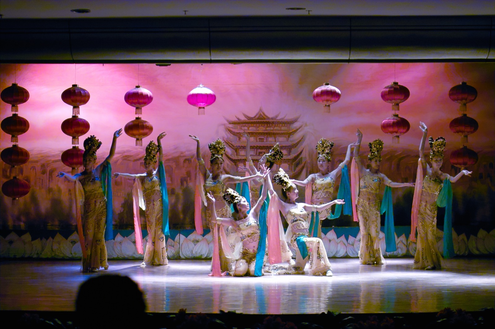 Dunhuang Silk Road dance performance — dancers in flowing mural-inspired silks under stage light, apsara poses from the cave paintings