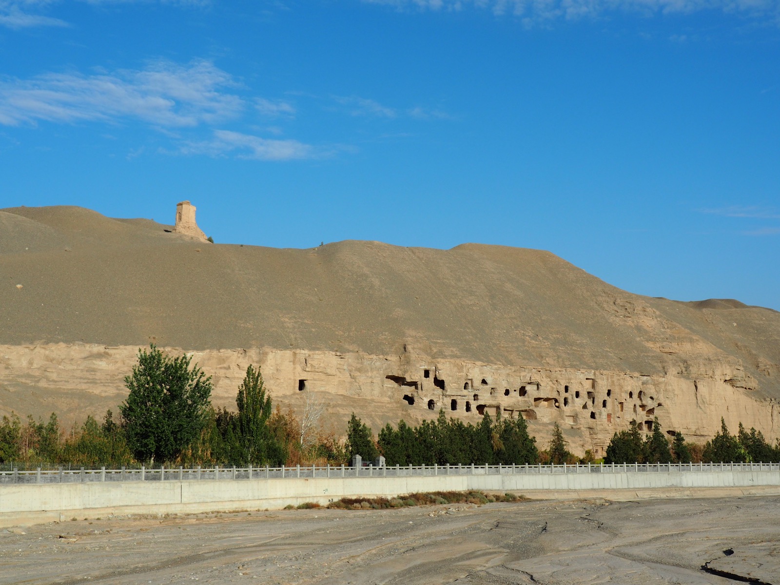 The honeycomb cliff face of the Mogao Caves, hundreds of grotto entrances stacked up the rock above the river valley