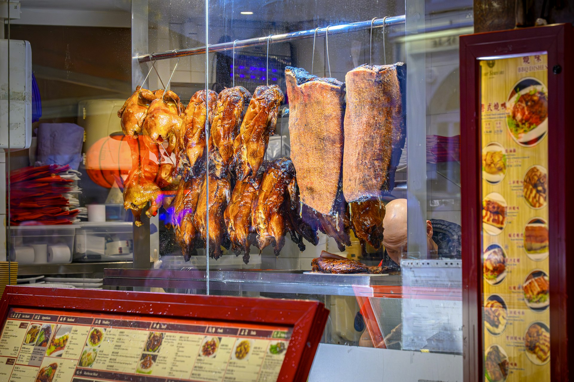 Cantonese roast goose and char siu hanging glossy in a Xiguan roast-meat shop window, cleaver mid-chop