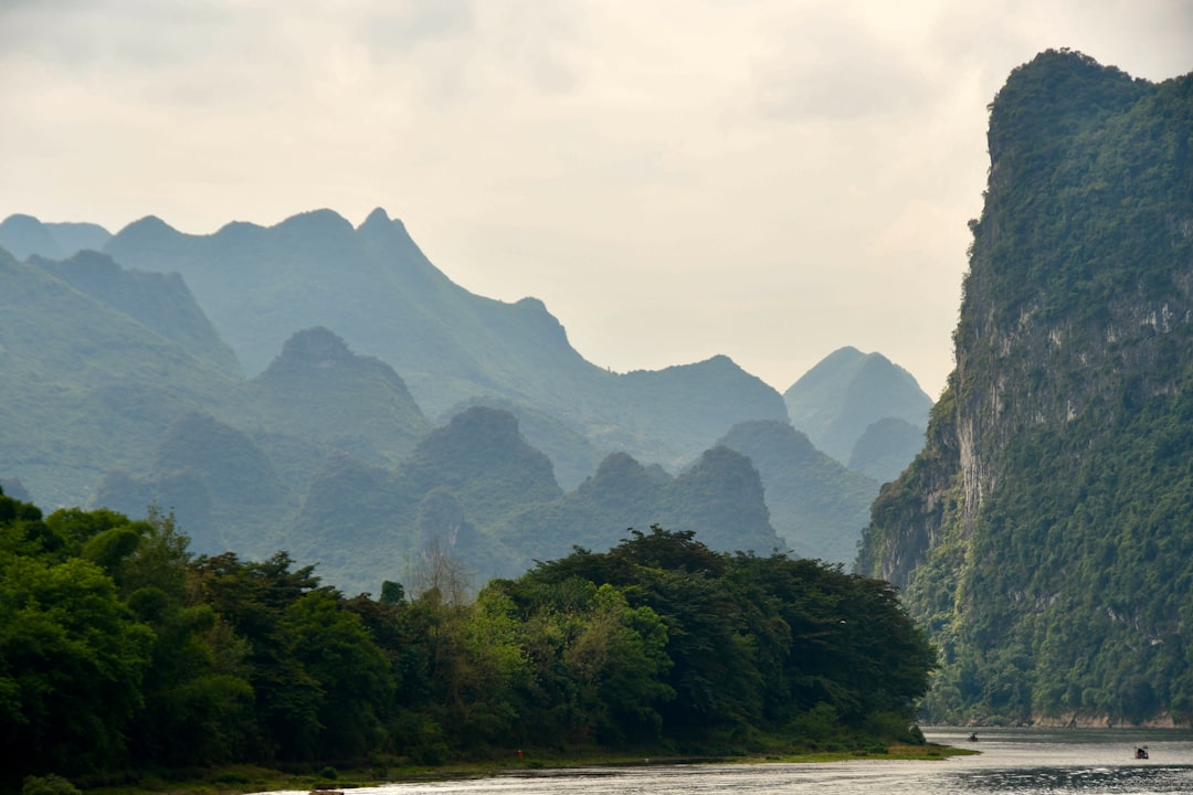 Li River at dawn — karst peaks rising from mist above jade-green water, a bamboo raft gliding through the foreground