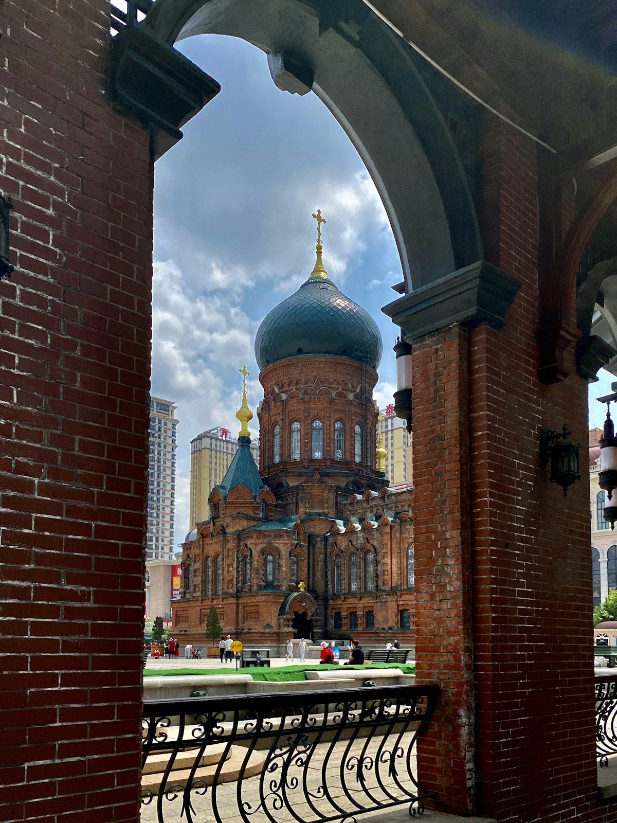 Saint Sophia Cathedral in snow — green Byzantine onion dome and red-brick walls against a grey winter sky, pigeons in the square