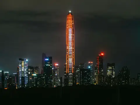 Shenzhen's Futian skyline at night — the Ping An Finance Centre outlined in orange light, spearing the low clouds above the CBD towers
