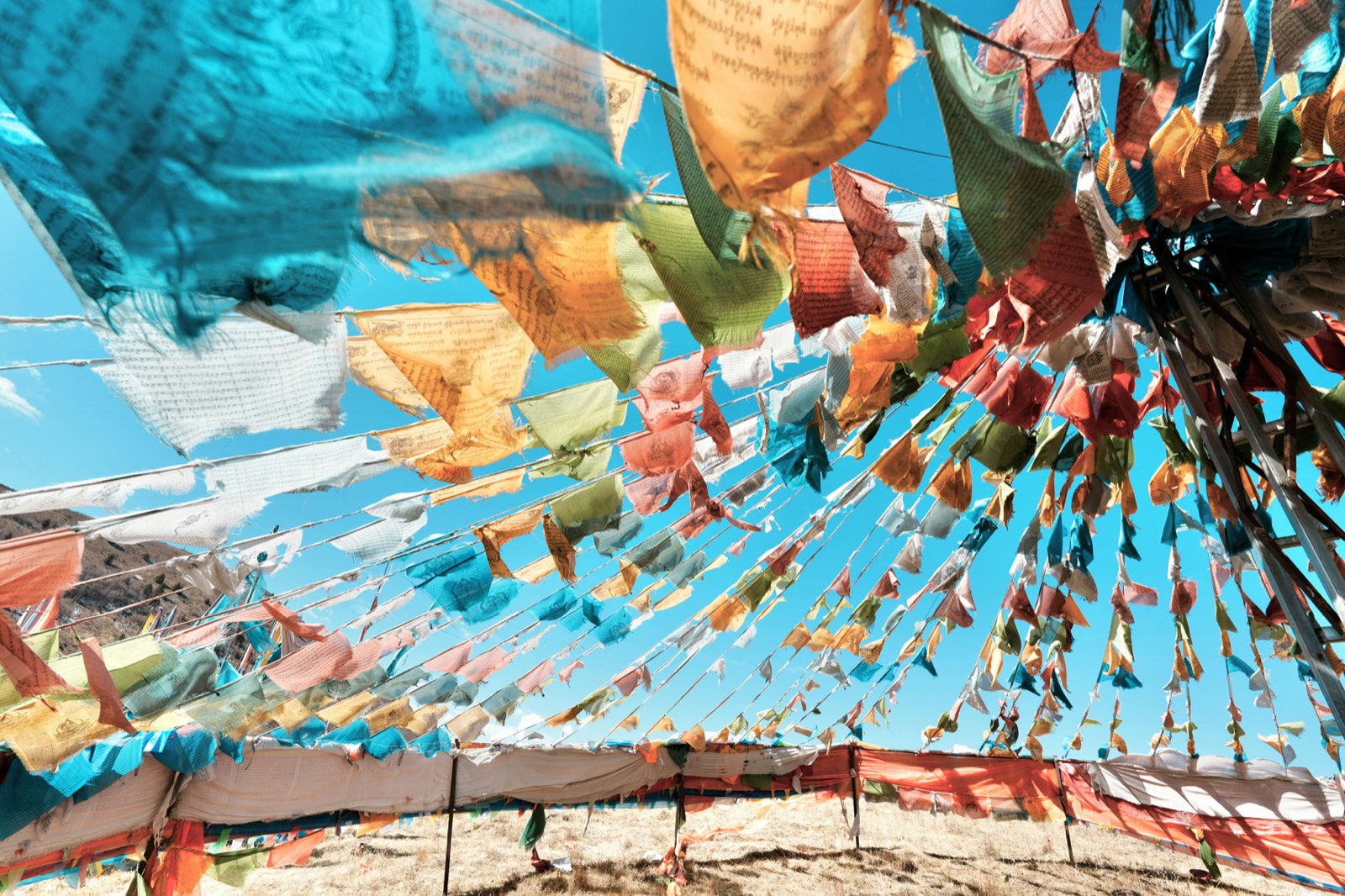 Strings of colourful Tibetan prayer flags flying against a blue sky above a dry hillside
