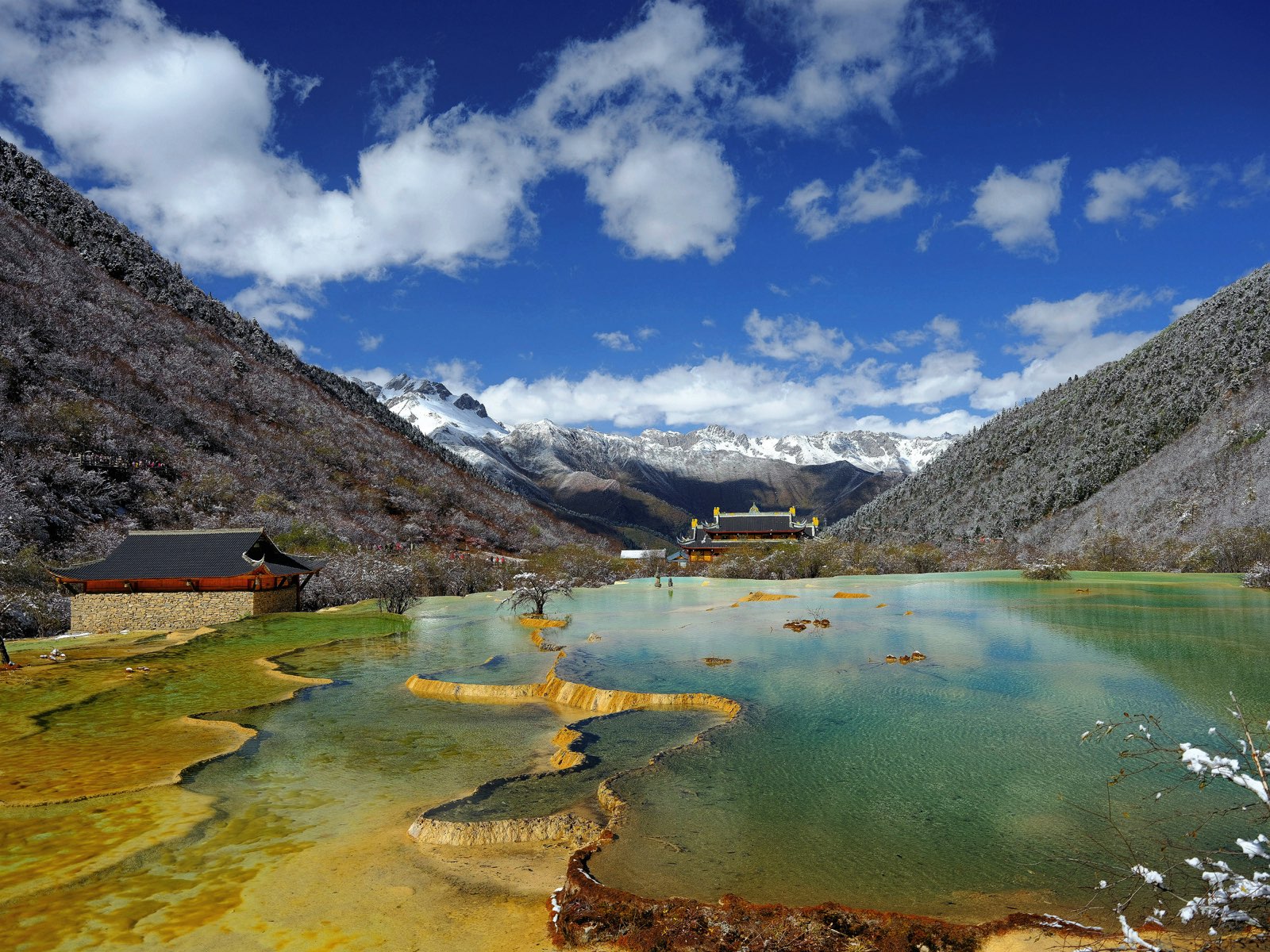 Colourful terraced pools at Huanglong with a temple and snow-capped peaks beyond