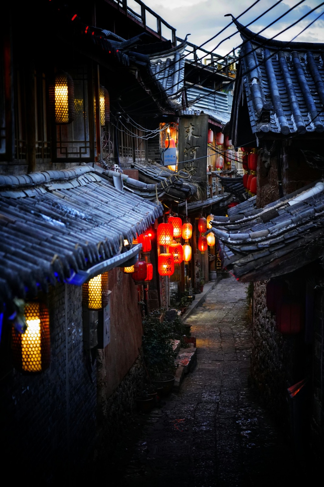 Lantern-lit cobblestone lanes and willow-lined canals in Lijiang Old Town at dusk, Naxi rooftops above