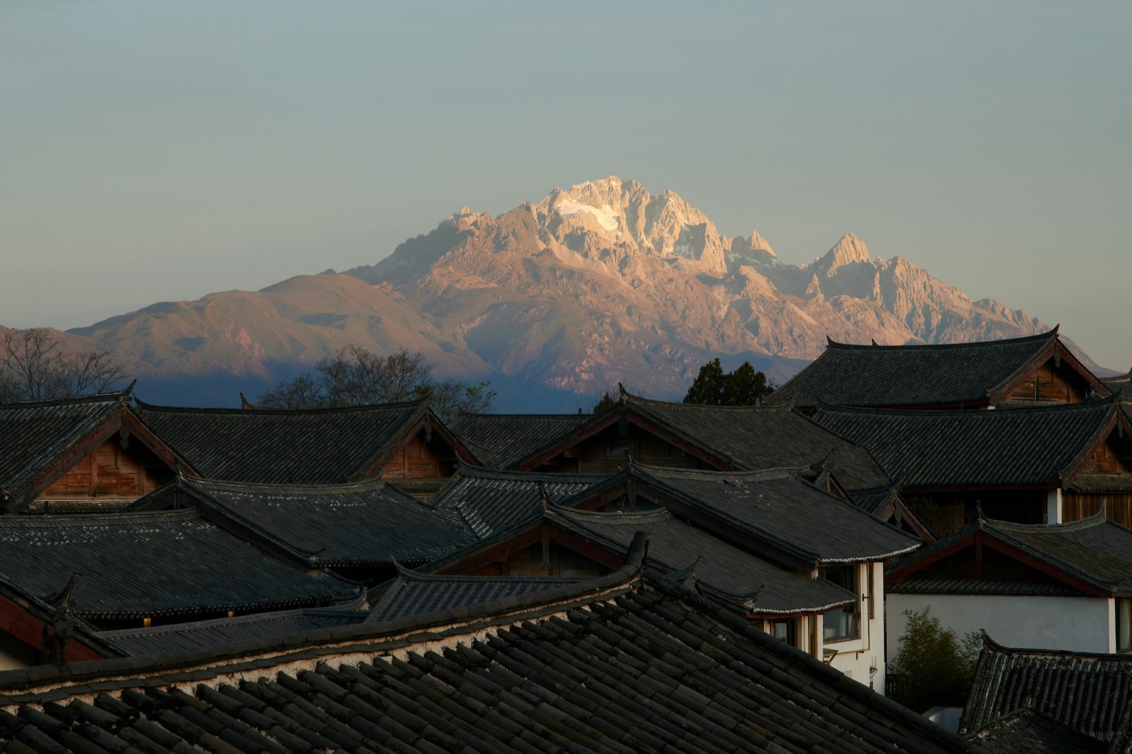 Jade Dragon Snow Mountain rising behind the grey-tiled rooftops and canals of Lijiang Old Town under a clear sky