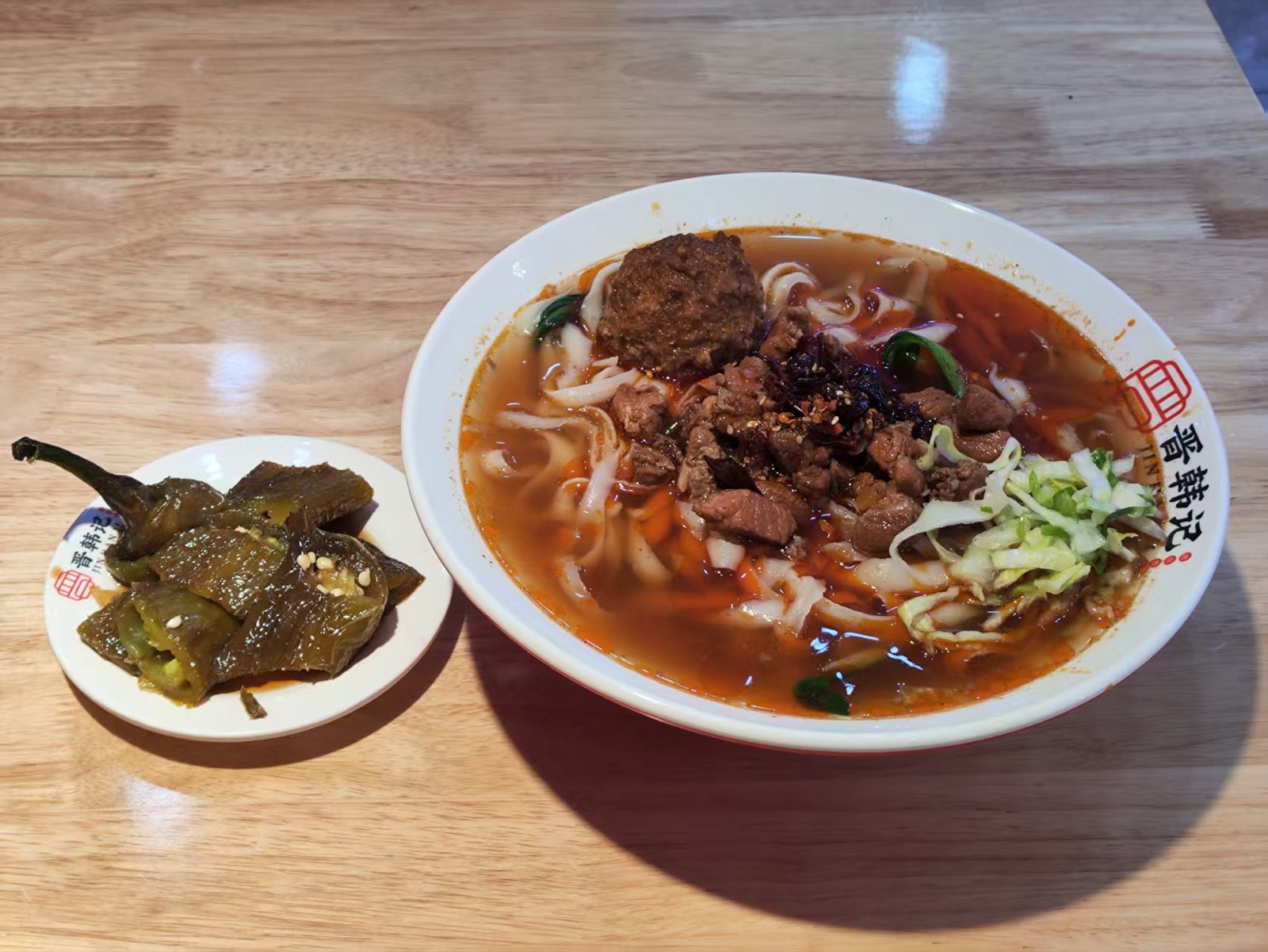 A bowl of Shanxi knife-cut noodles beside a plate of sliced Pingyao beef and a dish of dark aged vinegar