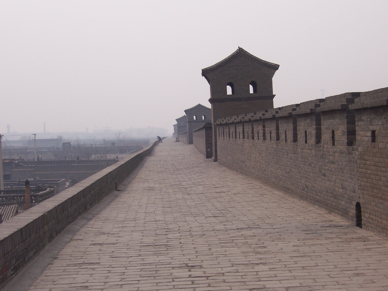 Walking atop Pingyao's Ming city wall at golden hour — crenellations, a watchtower, the grey-tiled old town below