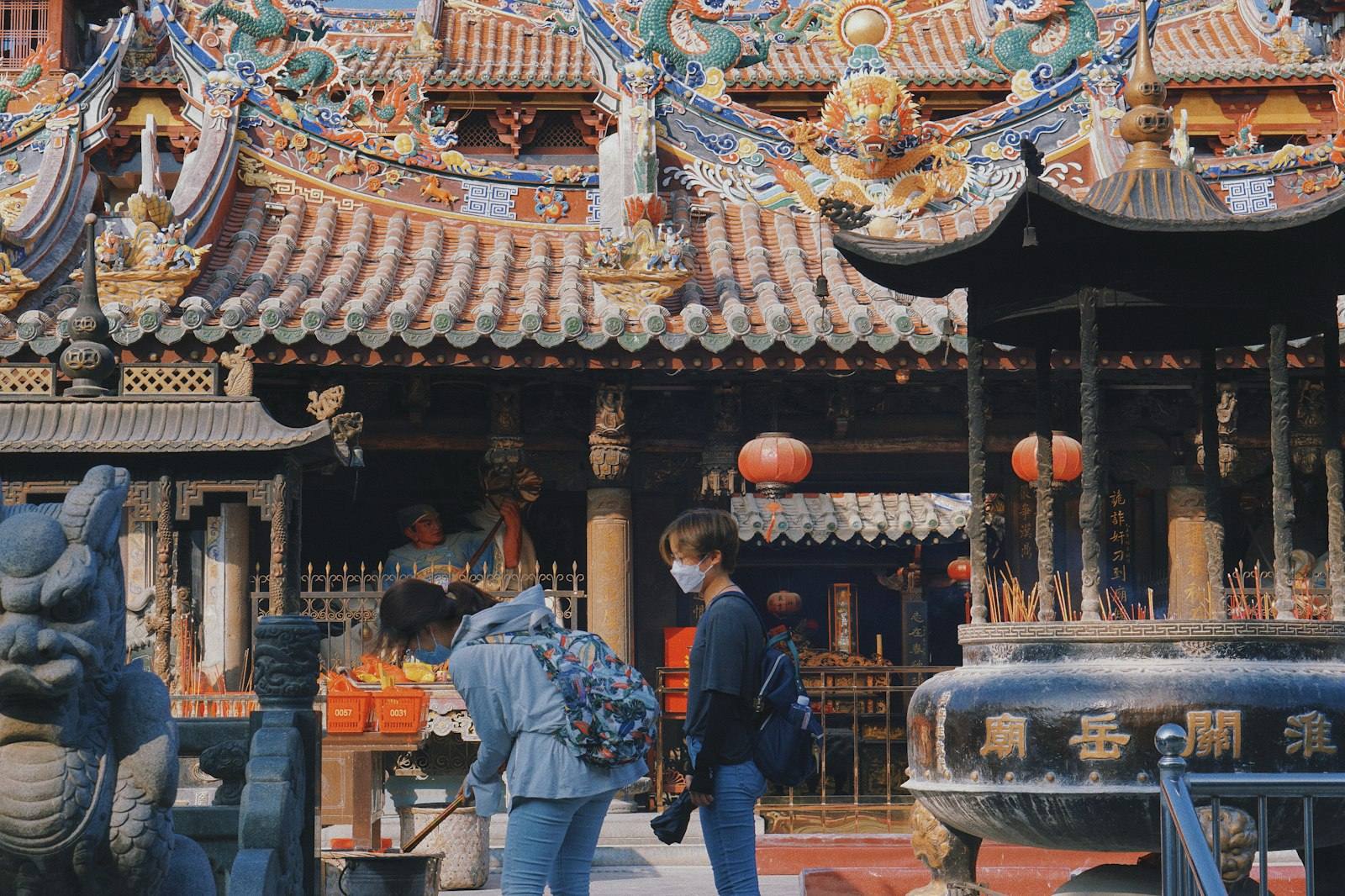 Visitors in the courtyard of Guandi (Guanyue) Temple on Tumen Street, Quanzhou — a big bronze incense burner filled with joss sticks at right, colourful dragons and figurines along the roof ridge behind