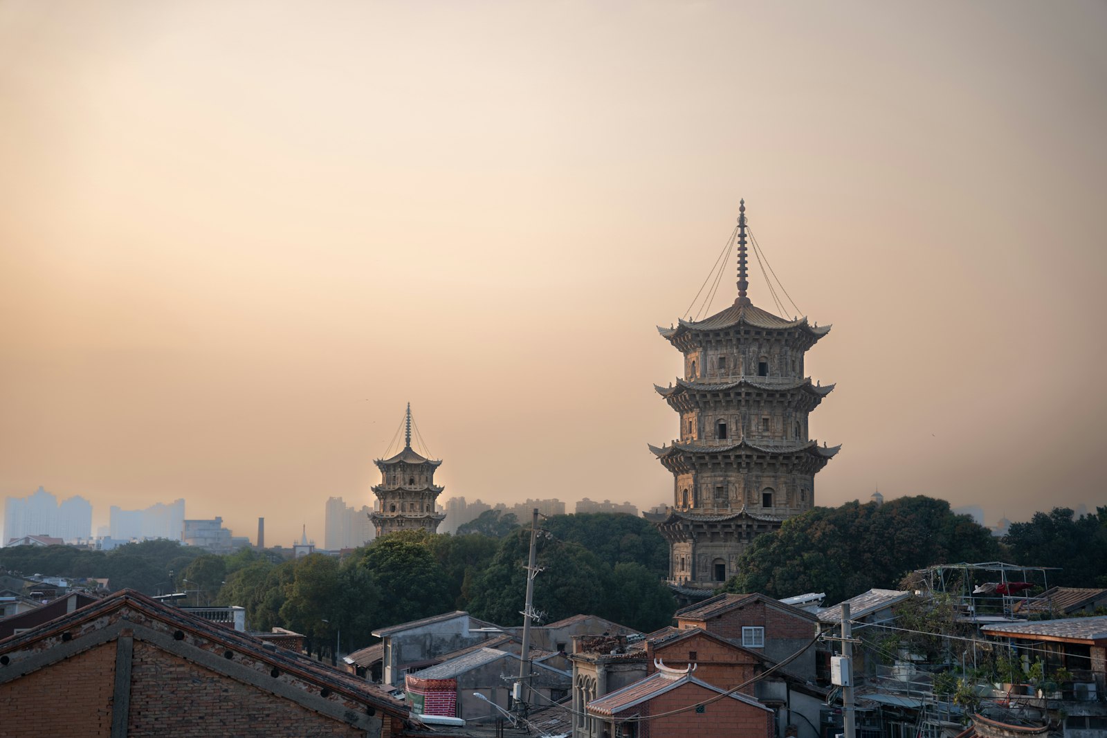 Kaiyuan Temple's two stone pagodas rising above the treetops in the warm haze of low sun, the taller one in the foreground and the shorter one beyond, Quanzhou