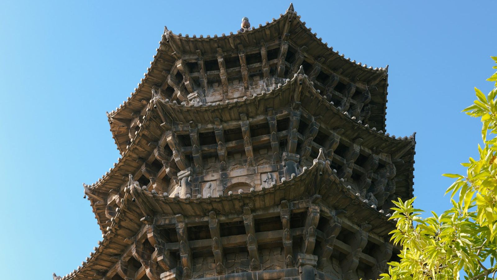 Close-up of one of Kaiyuan Temple's stone pagodas against a blue sky — tiers of upturned eaves, with brackets and beams carved from stone to imitate timber
