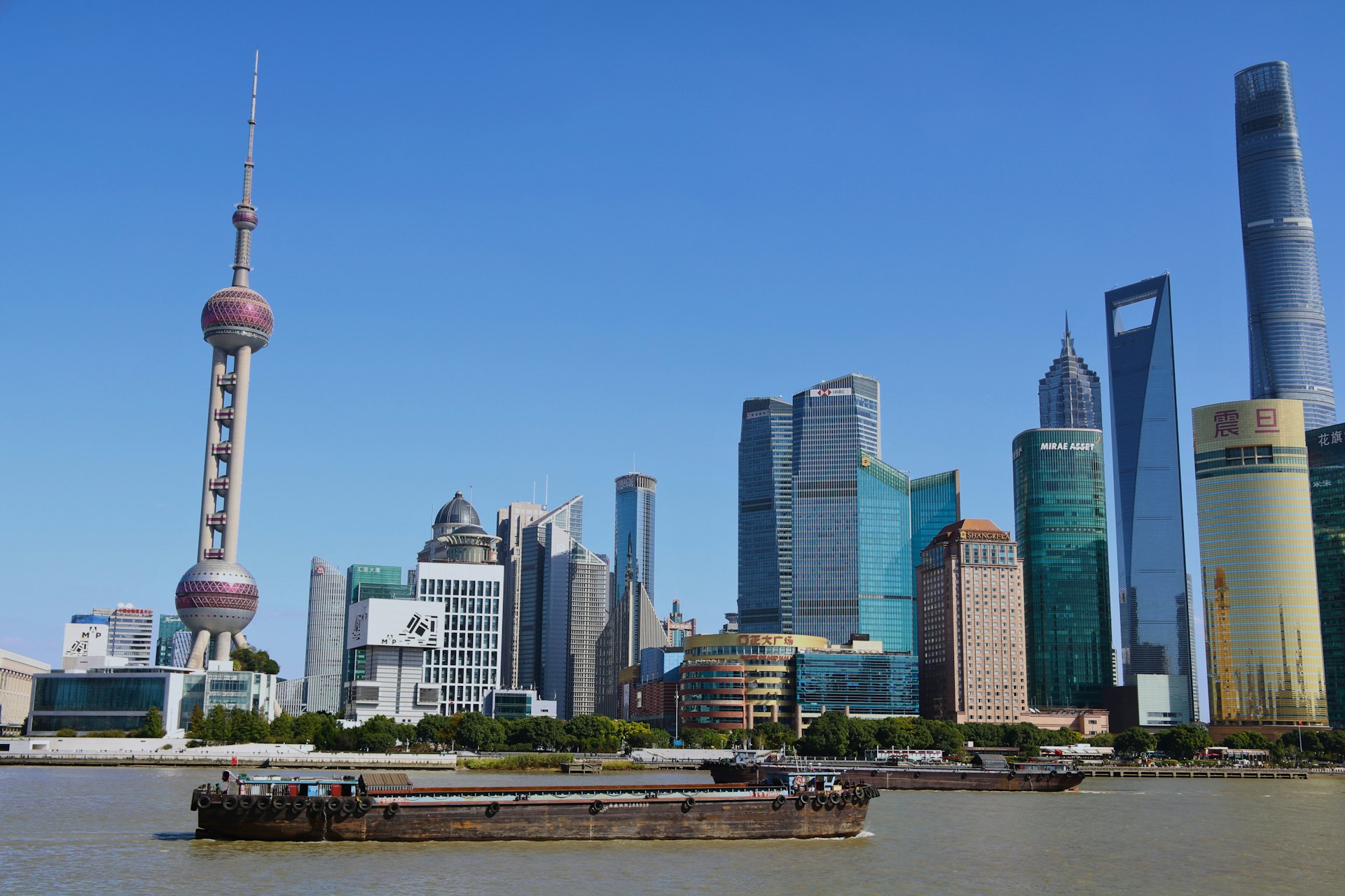 The Bund at dusk — colonial stone facades on the near bank, the lit-up Pudong skyline glowing across the Huangpu River