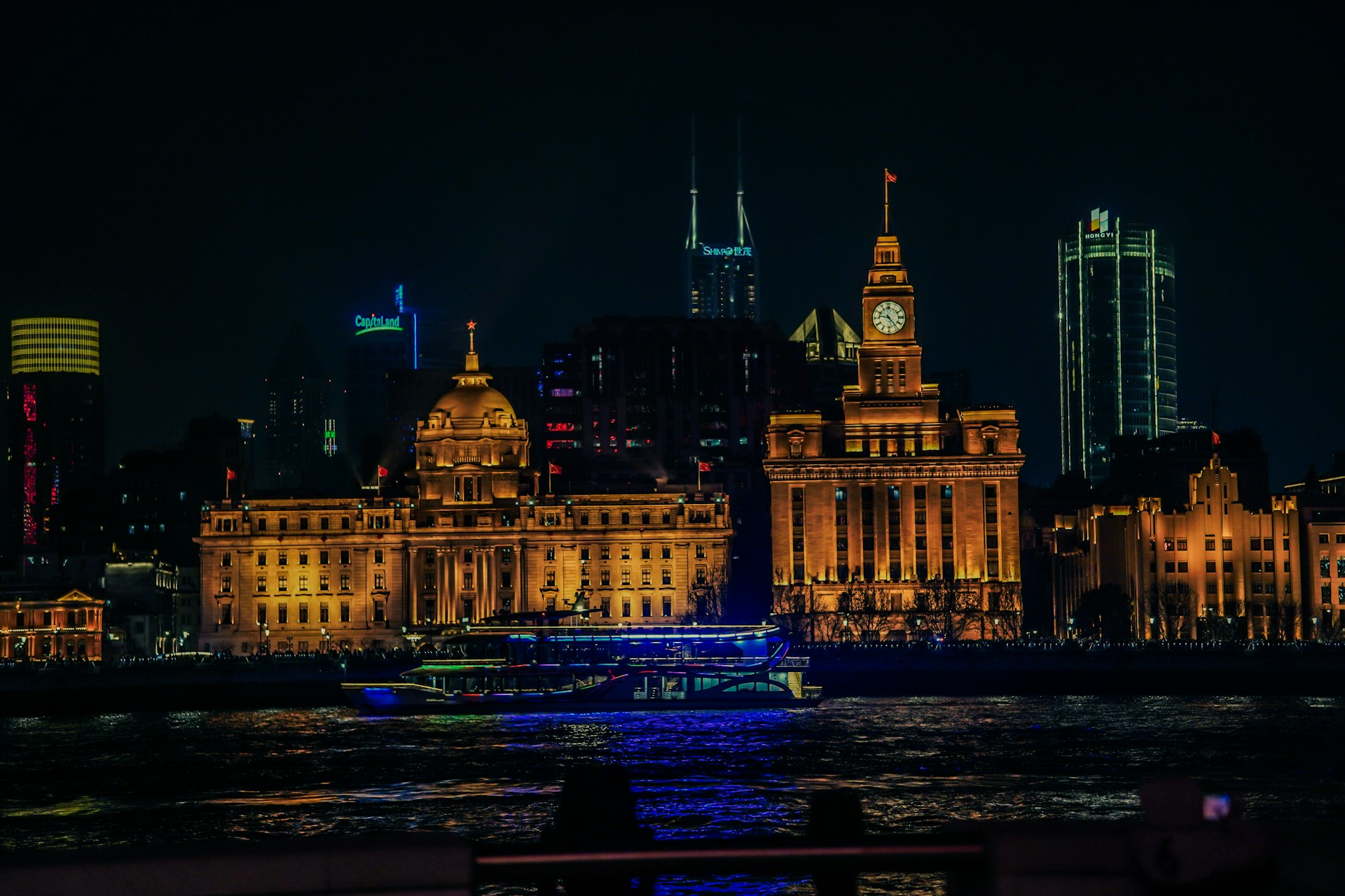 A Bund rooftop bar at night — cocktails on a terrace railing with the lit Pudong skyline filling the background across the river