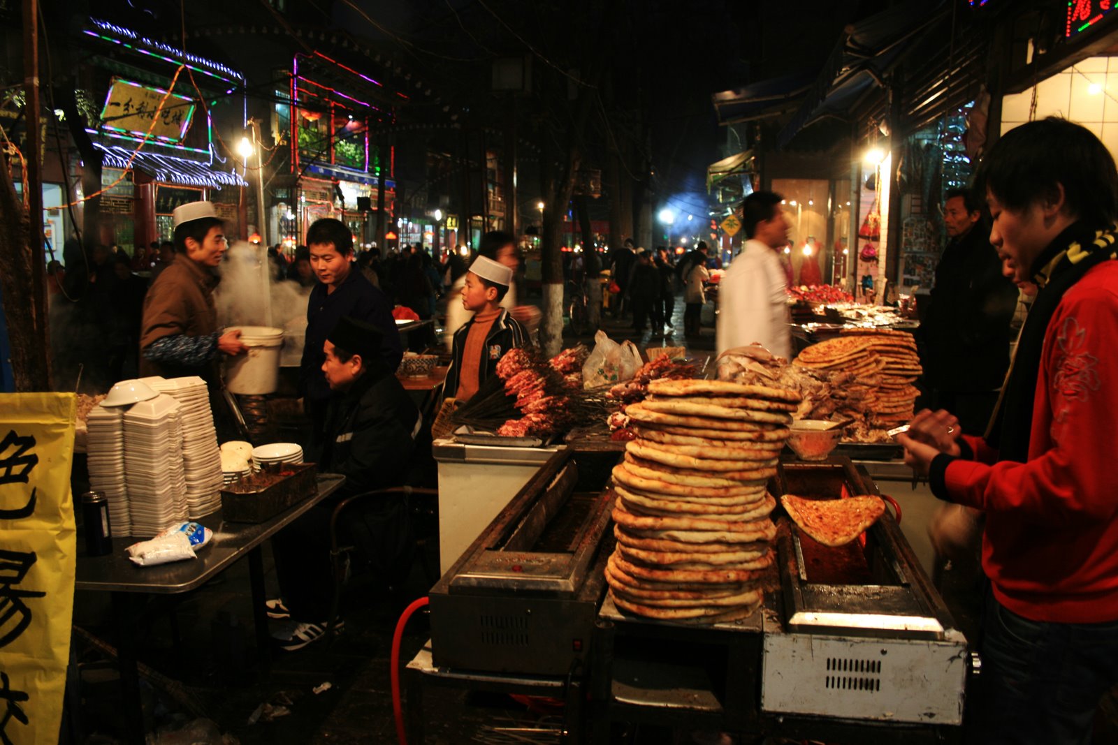 Night crowds and steaming food stalls along Xi'an's Muslim Quarter (Huimin Jie), lamb skewers grilling and roujiamo buns in the window